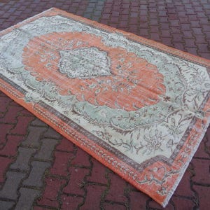 May include: A vintage rug with a floral pattern in shades of peach, cream, and grey. The rug has a distressed look and a fringed edge.