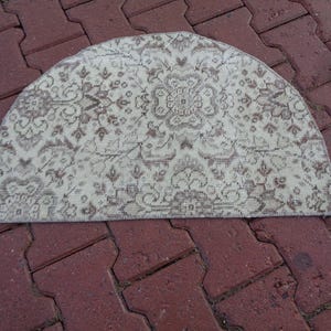 May include: A half-circle rug with a cream background and a brown floral pattern. The rug is made of a soft, woven material and has a fringed edge.