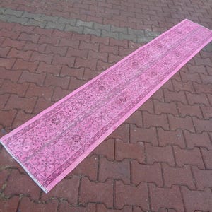 May include: A long pink runner rug with a floral pattern. The rug has a white fringe on the edges.
