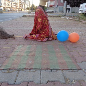 May include: A red and gold patterned robe with a long, brown broom lying on the ground. There are two balloons, one blue and one orange, on the ground.