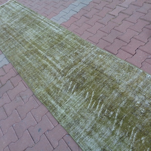 Könnte beinhalten: Ein langer, grüner und weißer Läuferteppich mit einem abgenutzten Look. Der Teppich ist aus einem weichen, gewebten Material gefertigt und hat ein dezentes Muster.