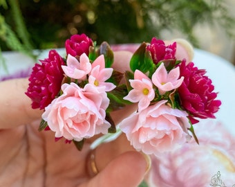 Peut inclure: Une paire de boucles d'oreilles florales avec de minuscules fleurs roses et magenta et des feuilles vertes. Les boucles d'oreilles sont conçues pour ressembler à un bouquet de fleurs.