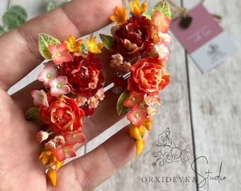 May include: A pair of handmade polymer clay earrings featuring cascading orange, red, and white flowers. The earrings are designed to resemble a bouquet of flowers.