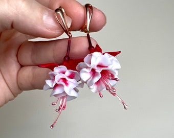 May include: A pair of earrings featuring white and red fuchsia flowers with gold-tone hooks.