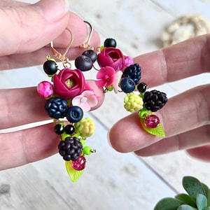 ベリーと花のアクセントがついた、一点もののポリマークレイ製ハンドメイドダングルイヤリング。ブラックベリーと花のモチーフが手作りされた、遊び心のあるジュエリーです。
