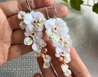 May include: A pair of dangle earrings featuring white orchid flower blossoms with pink accents. The earrings are made of polymer clay and have silver hooks.