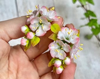 May include: A pair of delicate earrings featuring clusters of white and pink polymer clay flowers with yellow centers. The flowers are arranged in a cascading design, resembling cherry blossoms.