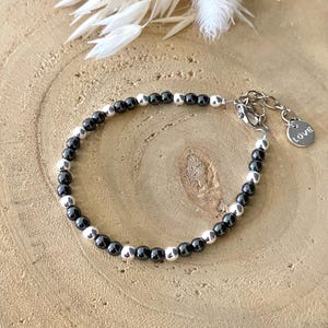 May include: A black and silver beaded bracelet with a silver clasp and a small silver charm that says "LOVE".