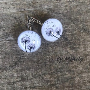 Può includere: Un paio di orecchini pendenti in argento con cabochon di vetro bianco che presentano un design di dente di leone nero. Gli orecchini hanno una chiusura a gancio in argento.
