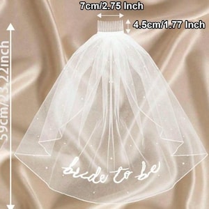 May include: A white bridal veil with the text "bride to be" in cursive. The veil is 59cm/23.22 inches long and 7cm/2.75 inches wide, with a comb that is 4.5cm/1.77 inches. The veil is decorated with small, scattered pearls.