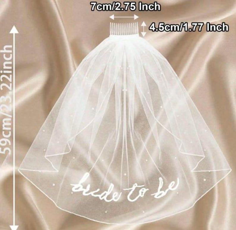 May include: A white bridal veil with the text "bride to be" in cursive. The veil is 59cm/23.22 inches long and 7cm/2.75 inches wide, with a comb that is 4.5cm/1.77 inches. The veil is decorated with small, scattered pearls.