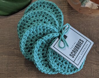 May include: Set of five teal crocheted facial scrubbies with a tag that reads "Facial Scrubbies 100% Handmade"