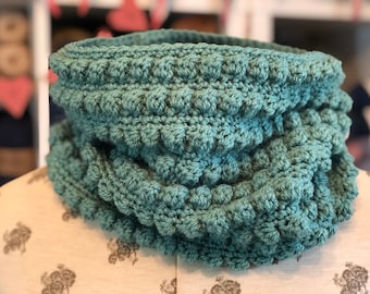 May include: A teal blue crocheted infinity scarf with a textured, bumpy design.