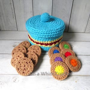 May include: A crocheted blue cookie jar with a red and yellow stripe, and a small ball on top. Several crocheted cookies are arranged around the jar. Some cookies have colorful centers. The text "On a Whim Crochet" is visible.