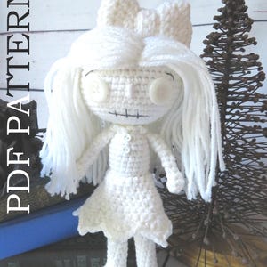 May include: A handmade white crochet doll with button eyes, long white hair, and a bow. The doll is wearing a dress and has a stitched mouth. The words "PDF PATTERN" are printed vertically on the left side of the image.