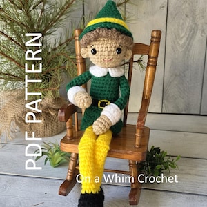 Könnte beinhalten: Eine gehäkelte Elfenpuppe mit grün-gelbem Hut, grünem Outfit und gelber Hose, die in einem Miniatur-Schaukelstuhl aus Holz sitzt. Die Puppe hat ein lächelndes Gesicht und schwarze Schuhe. Der Text "PDF PATTERN" und "On a Whim Crochet" sind sichtbar.