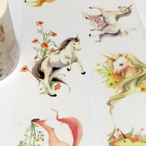 May include: A roll of washi tape featuring a repeating pattern of white unicorns with floral accents. The unicorns are surrounded by flowers in shades of pink, yellow, and orange. The tape is on a white background.