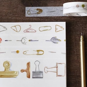 以下が含まれることがあります： 様々な金と銀のオフィス用品、クリップ、安全ピン、洗濯ばさみなど、繰り返しのパターンを持つ和紙テープのシート。テープは白い背景の上にあります。