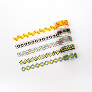 Puede incluir: Seis rollos de cinta washi estampada de colores. La cinta presenta diseños geométricos en amarillo, naranja, azul, verde y negro.