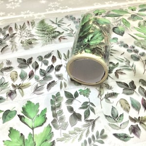 May include: A roll of clear washi tape with a repeating pattern of green watercolor leaves. The tape is on a white background with a lace pattern.