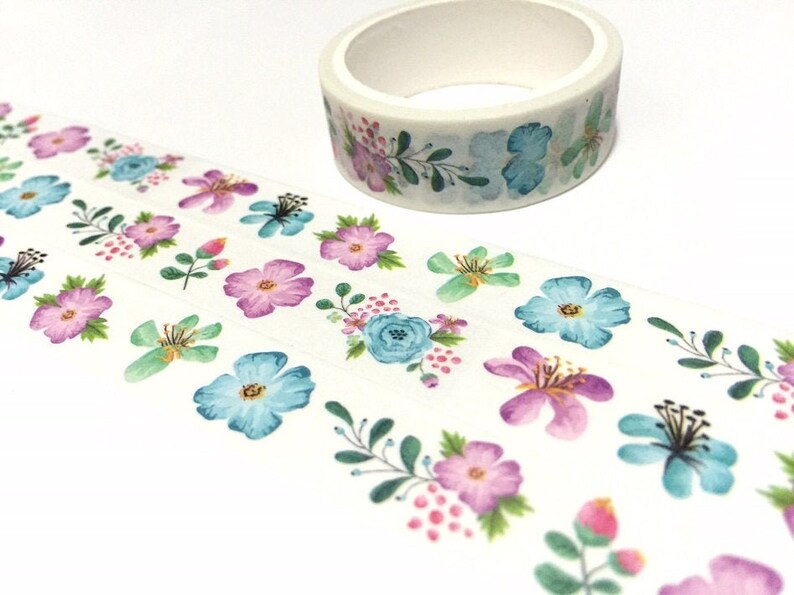 May include: A roll of washi tape with a floral pattern. The tape features blue, pink, and green flowers on a white background.