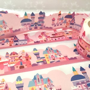 Puede incluir: Cinta washi rosa y blanca con un patrón repetido de castillos de dibujos animados coloridos. La cinta está enrollada y lista para usar.