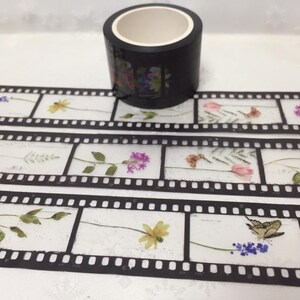 Może przedstawiać: Czarna rolka taśmy washi z kwiatowym wzorem. Taśma ma wz&oacute;r taśmy filmowej z r&oacute;żnymi kwiatami, motylami i zielenią. Idealna do scrapbookingu, prowadzenia dziennika i innych prac ręcznych.