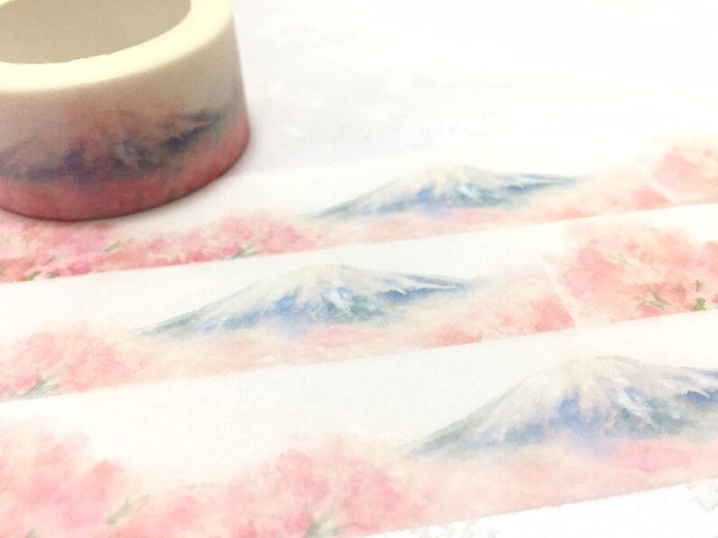 K&ouml;nnte beinhalten: Eine Rolle Washi-Tape mit einem Aquarell-Design von Mount Fuji und Kirschbl&uuml;ten. Das Band ist wei&szlig; mit einem hellrosa und blauen Aquarell-Design.