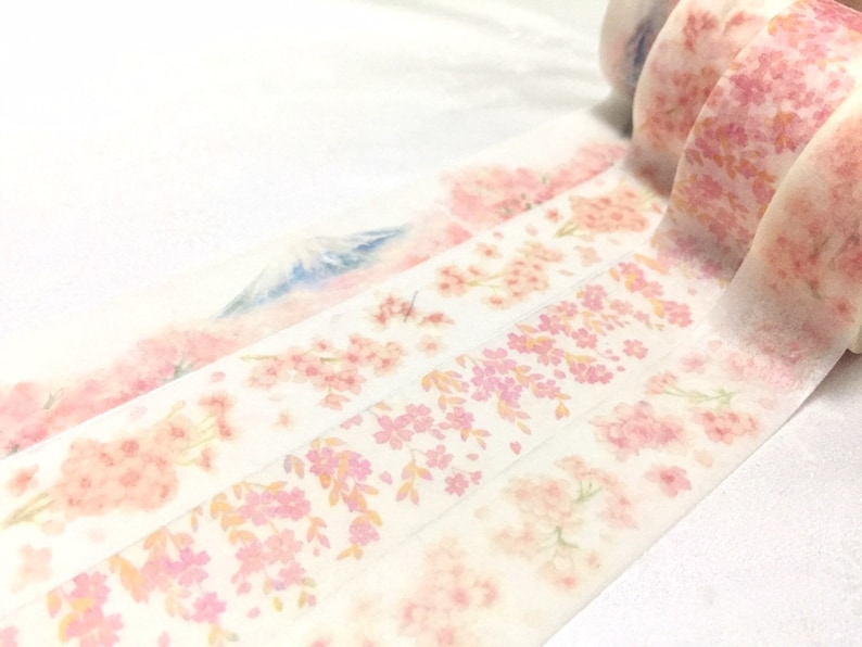 K&ouml;nnte beinhalten: Eine Rolle dekoratives Washi-Tape mit einem zarten Blumenmuster in Rosa- und Wei&szlig;t&ouml;nen. Das Band hat einen dezenten Aquarelleffekt und ein Kirschbl&uuml;tenmuster.