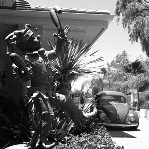 Könnte beinhalten: Ein Schwarzweißfoto einer Gauklerstatue, die einen Jonglierstab hält. Die Statue steht auf einer großen, runden, weißen Kugel. Ein schwarz-weißer Volkswagen Käfer ist im Hintergrund geparkt.
