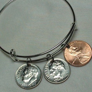 May include: A silver bangle bracelet with three charms: two silver dimes from 2012 and one copper penny from 2012.