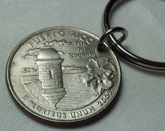 May include: A Puerto Rico quarter coin attached to a silver-colored key ring. The coin features a fort, a flower, and the inscription "Puerto Rico" and "E Pluribus Unum". The key ring is a simple, round design.