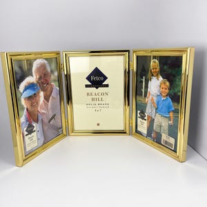 May include: A gold-toned metal triple folding picture frame with a polished finish. The center frame contains a white insert with the text Fetco International Beacon Hill Solid Brass Lacquer Coated 5 x 7. The side frames hold photographs.