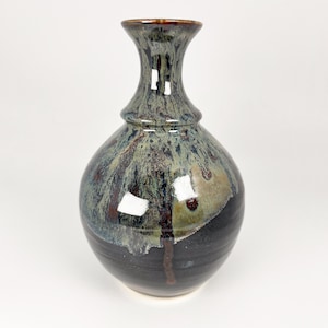 May include: A ceramic vase with a bulbous body and a narrow neck. The glaze features a blend of deep black at the base, transitioning into a mottled pattern of sage green, blue, and brown tones that drip downward from the rim toward the centre.