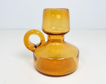 May include: Amber-colored glass pitcher with a rounded base, a cylindrical top, and a circular handle. The pitcher is made of transparent glass, allowing light to pass through. The design is simple and elegant, suitable for serving beverages or as a decorative item.