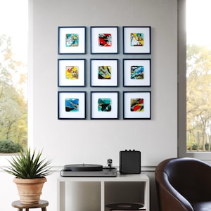 May include: Nine framed abstract art prints with colorful designs hang on a wall. A white cube shelf holds a record player, speaker, and vinyl records. A potted plant sits on a wooden stool.