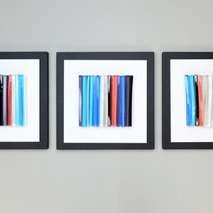 Pu&ograve; includere: Tre pezzi di arte da parete incorniciati con motivi a mosaico di vetro colorati. Ogni pezzo presenta una disposizione verticale di bacchette di vetro in tonalit&agrave; di blu, rosso, bianco e nero.