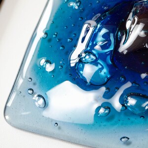 May include: A square glass plate featuring a gradient of blue tones, ranging from light sky blue to deep navy. The surface is textured with numerous raised, clear, bubble-like inclusions of varying sizes, creating a three-dimensional effect.