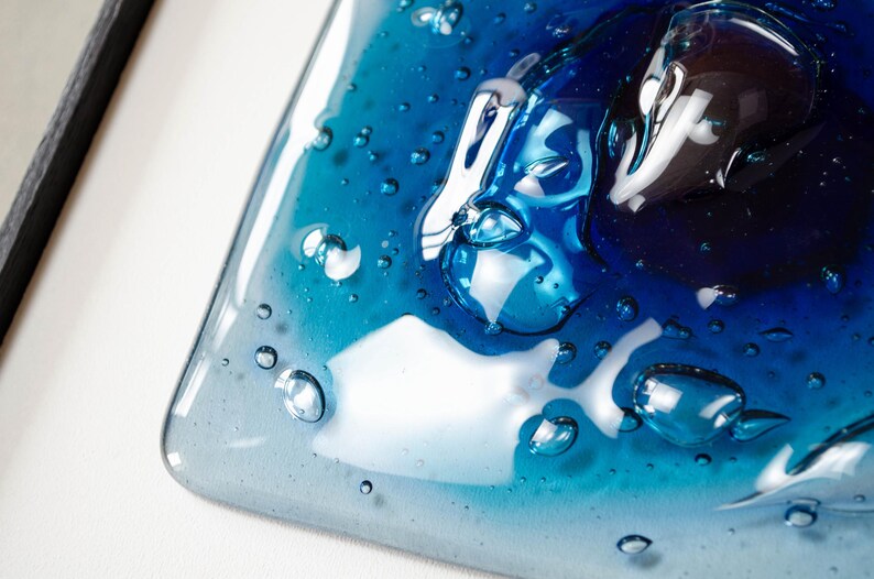 May include: A square glass plate featuring a gradient of blue tones, ranging from light sky blue to deep navy. The surface is textured with numerous raised, clear, bubble-like inclusions of varying sizes, creating a three-dimensional effect.