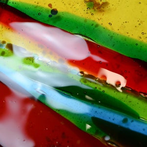 K&ouml;nnte beinhalten: Nahaufnahme einer bunten Glasschale mit Streifen in Rot, Gr&uuml;n, Blau und Gelb. Das Glas hat eine strukturierte Oberfl&auml;che mit kleinen Luftblasen.