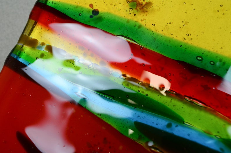 K&ouml;nnte beinhalten: Nahaufnahme einer bunten Glasschale mit Streifen in Rot, Gr&uuml;n, Blau und Gelb. Das Glas hat eine strukturierte Oberfl&auml;che mit kleinen Luftblasen.