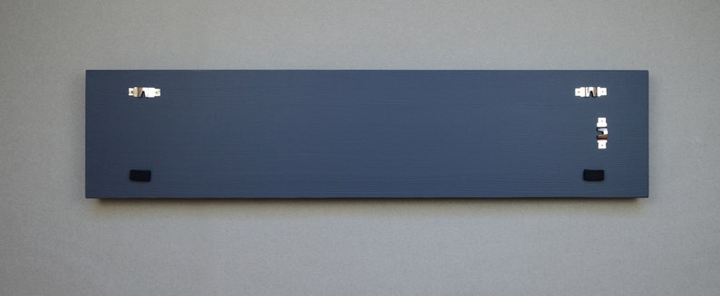 May include: A dark gray rectangular sign with four silver hanging hooks and two black hanging hooks.