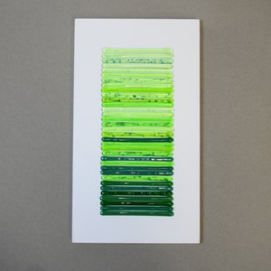 May include: A white rectangular frame with a vertical row of 25 green glass tubes, each with a different shade of green.