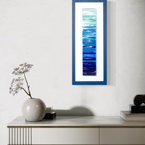 May include: A framed wall art piece with a gradient of blue glass tiles, ranging from light blue to dark blue, creating a vertical ombre effect.