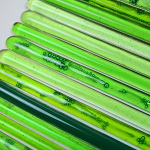 May include: A collection of green glass rods with air bubbles trapped inside. The rods are arranged in a diagonal pattern, creating a gradient of green shades.