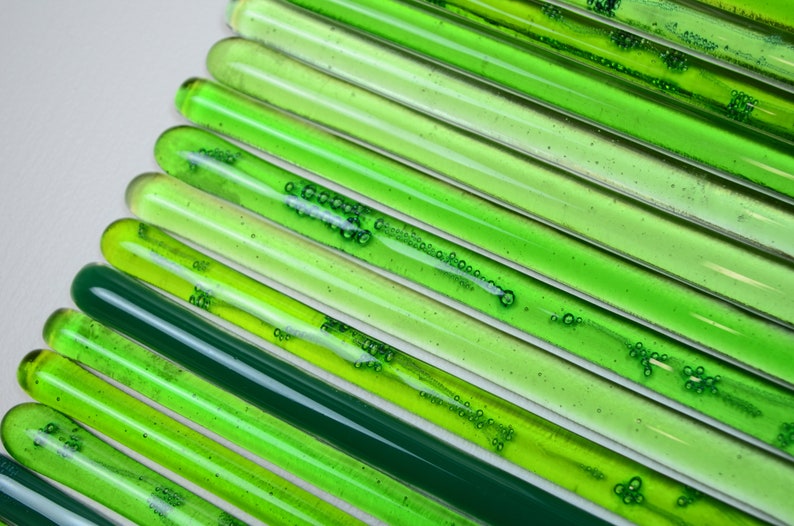 May include: A collection of green glass rods with air bubbles trapped inside. The rods are arranged in a diagonal pattern, creating a gradient of green shades.