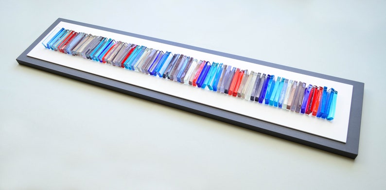 May include: A framed wall art piece featuring a long row of colorful glass rods in shades of blue, red, and gray. The rods are arranged in a staggered pattern, creating a dynamic and modern look.