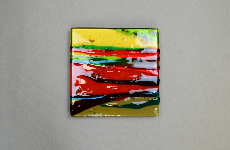 K&ouml;nnte beinhalten: Eine quadratische Glasfliese mit einem mehrschichtigen Design aus rotem, gr&uuml;nem, blauem und gelbem Glas. Das Glas ist durchscheinend und hat eine gl&auml;nzende Oberfl&auml;che.