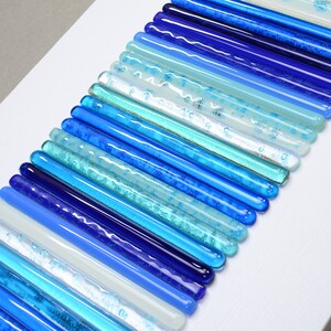 Pu&ograve; includere: Un'opera d'arte da parete realizzata con bacchette di vetro in varie tonalit&agrave; di blu, bianco e acquamarina. Le bacchette sono disposte in un motivo curvo, creando un effetto sfumato.
