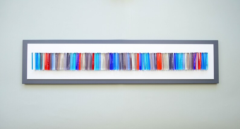 May include: A framed wall art piece featuring a horizontal row of colorful glass rods in shades of blue, red, and gray. The rods are arranged in a random pattern, creating a modern and abstract design.